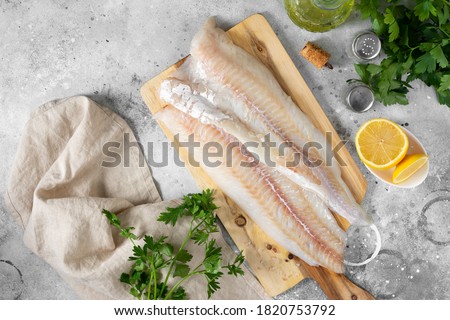 Raw cod fish fillet on a chopping Board on a light gray kitchen table. Preparation for cooking fish. Top view	