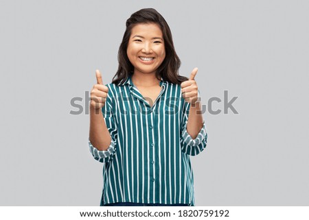 people, gesture and portrait concept - happy asian young woman showing thumbs up over grey background