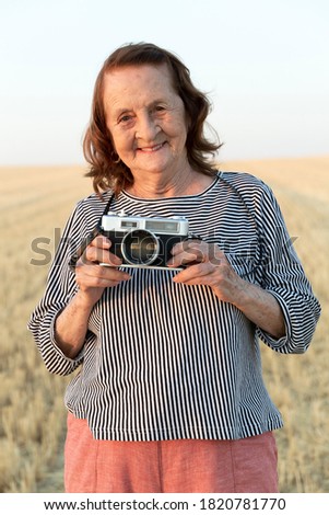 Portrait of an elderly woman with an analog camera in the field.