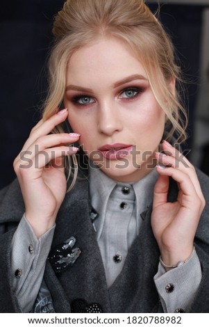 close up portrait of elegant rich lady in woolen grey coat is posing on blue fabric background in studio. indoor photo of fashionable, stylish woman with makeup and hairstyle, glamour style, vogue
