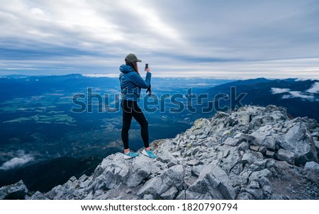 Mobile phone selfie hiker taking photo or video with cellphone in fog in mountain panorama background. Nature walk recreational activity girl happy using tech device. Outdoor fall lifestyle