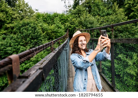 Traveler girl is taking a photo of nature on the smartphone. A woman in casual wear with a phone on the bridge