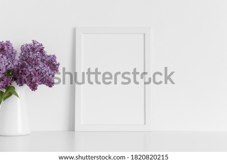 White frame mockup with a bouquet of lilac in a vase on a white table.Portrait orientation.