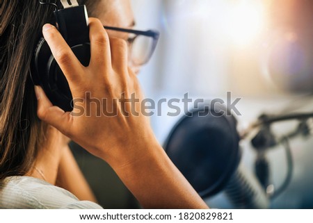 Young Woman Hosting an online talk show from her studio, wearing headphones, talking to the microphone, side view