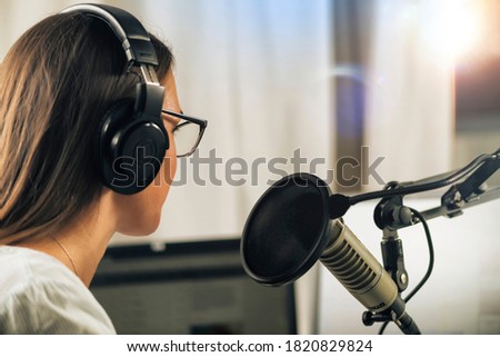 Young Woman Hosting an online talk show from her studio, wearing headphones, talking to the microphone, side view