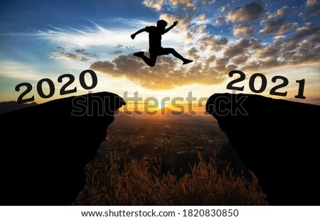 A young man jump between 2020 and 2021 years over the sun and through on the gap of hill  silhouette evening colorful sky. happy new year 2021. Royalty-Free Stock Photo #1820830850