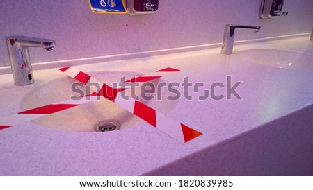 Bathroom sink with white red cordon tape in public toilet. Social distance requirements for washing hands. Virus protection. Sanitary rules. Washroom. Barrier rope. Illness Prevention. Purple lighting