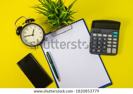 Minimal workspace concept: alarm clock, pen, notepad, calculator and smartphone, composition on yellow background. Flat top view. Copy space.