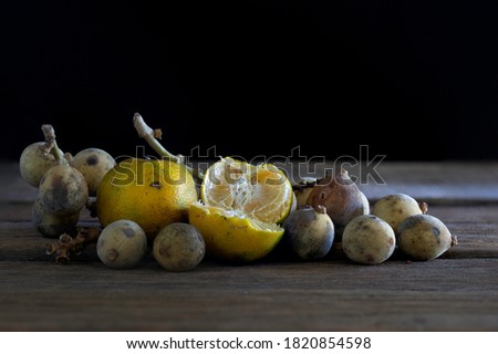 Oranges and Longkong (thai fruit) rotten and withered fruits with fungus and fruit fly on old wooden table which has black background  /  Select focus, still life image, space for text

