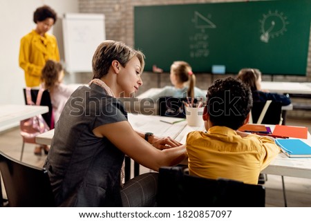 Female teacher helping elementary student with studying in the classroom.  Royalty-Free Stock Photo #1820857097