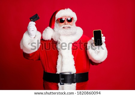 New pay opportunity. Photo of pensioner old man grey beard hold credit card telephone smile empty space wear x-mas santa costume gloves coat belt sunglass cap isolated red color background