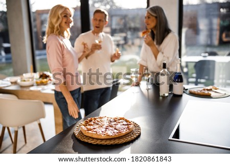 Delicious pizza on the table in the kitchen with adult people on the background in a cozy home
