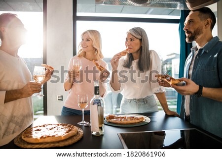 Smiling men and women talking while eating pizza and drinking wine in the kitchen stock photo