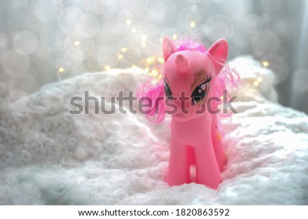 Toy pink pony unicorn on a light fur background with glittering lights and bokeh circles.