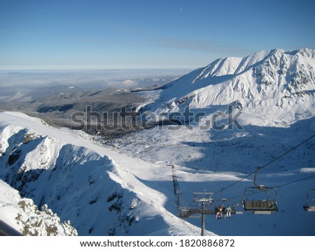 Panoramic view of snow-covered ski slope in Western Tatras at Kasprowy Wierch ski resort, Poland. Winter landscape on a clear sunny day with blue skies and a ski lift going up.