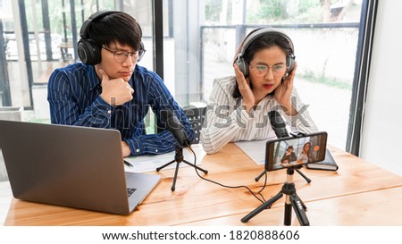 Asian Man and woman podcasters in headphones recording content with colleague talking to microphone and camera in broadcast studio together, communication technology and entertainment concept