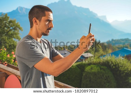 Young business man with mobile phone on beautiful scenic mountain background. Business man working in a rural hotel. Freelancer. Traveler. Taking pictures. 