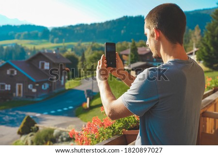 Young business man with mobile phone on beautiful scenic mountain background. Business man working in a rural hotel. Freelancer. Traveler. Taking pictures. 