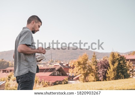 Young man with flying drone over  sunny green nature. Man operating a drone with remote control taking aerial photos and videos. Adventure concept. 