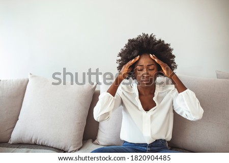 Woman suffering from a headache and rubbing her temples at home. African American woman having a headache. 
