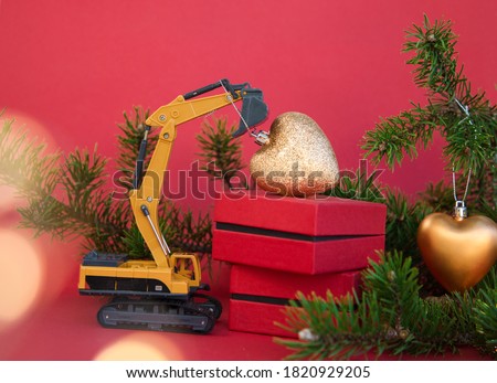 coniferous branch, bokeh, gift boxes, model of toy excavator, heart-shaped Christmas ball hanging on excavator's boom. Concept for Christmas construction business greetings