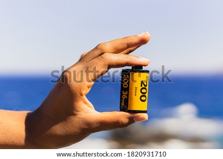 Unrecognizable brand 35mm film held in one hand against a summery, well lit background. Analog photography concept.