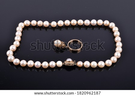 A white pearl necklace on a black reflective surface with a black background