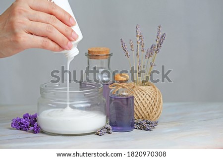 Crop hand pouring white lotion with lavender flower and essentai oil.