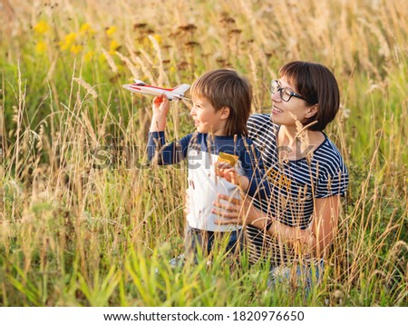 Cute boy and his mother play with toy airplane. Happy kid dreams to be a pilot. Boy is planning for the future. Mom and son on field at golden sunset hour at autumn season.