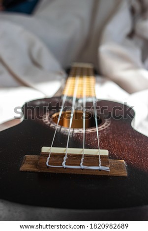 Photo of a brown ukelele lying on a bed with white sheets