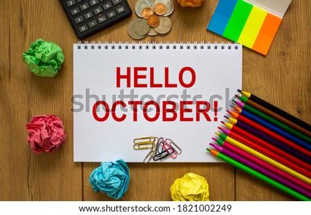 White note with inscription 'hello october' on beautiful wooden table, colored paper, colored pencils, paper clips, coins and calculator. Business concept.