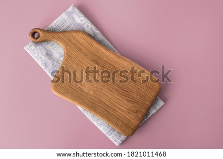 Close up of empty wooden cutting board lying on cotton napkin or towel placed on soft pink background, top view. Photography for menu card or cookbook with recipes.