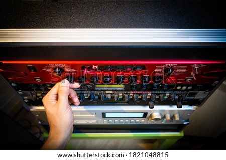 sound engineer hand tweaking knobs of studio gears, pre-amp, audio interface, effect signal processor for TV radio broadcasting, post production or music concept