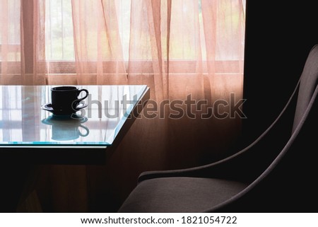 Corner of a modern apartment, consisting of a coffee table, sofa, and a large window as a backdrop covered with soft colored curtains.