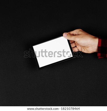 Photo frame in hands on black background. Preparation for text, mockup, copy space.