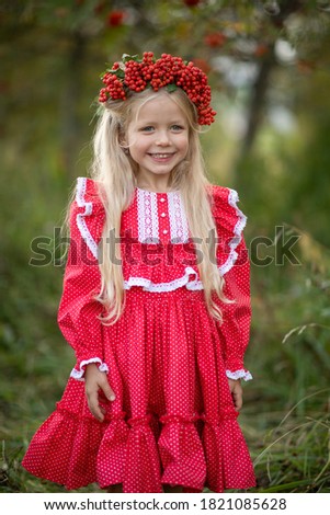 Portrait of a girl in the park. Girl in a red dress. The girl has a rowan wreath on her head. Image with selective focus.
