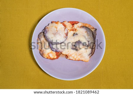 Aubergine parmigiana served in a lilac colored dish placed on a light green table runner, food photography of a typical Italian dish