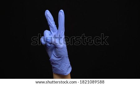 Female hand in a latex medical glove makes an peace gesture isolated on black background.