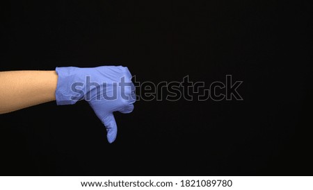 Female hand in a latex medical glove makes an unlike gesture isolated on black background.
