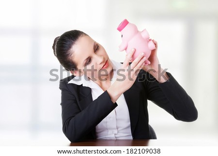 Happy business woman with her savings in piggy bank at the desk