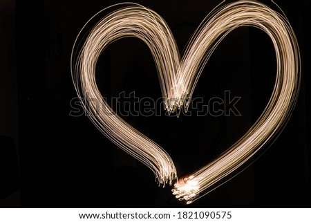 Long exposure photo of light trails making a heart shape on a black background with led lights