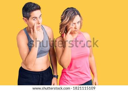 Couple of women wearing sportswear pointing to the eye watching you gesture, suspicious expression 