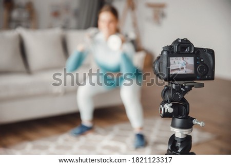 Video recording of online sports training on camera, woman performs fitness exercises home on background of kitchen.