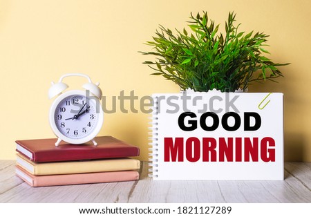 GOOD MORNING written on a white card near the diaries, alarm clock and green plant