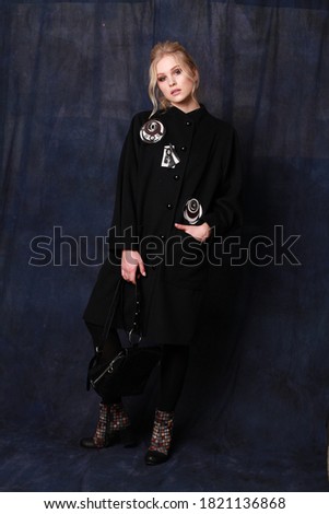 Stylishly dressed young woman in a smart casual look: black dress decorated with brooch posing in the studio. Vertical full-height image.