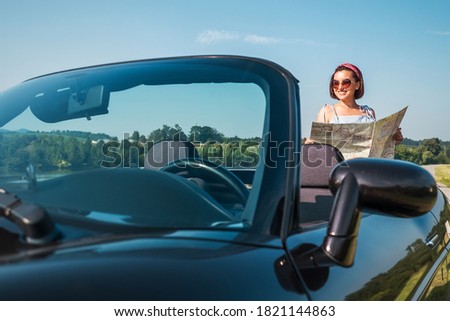 Woman looking a right road in the roadmap during her auto travel in the convertable cabriolet car. Traveling and navigation concept image.