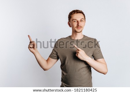 Portrait of a cheerful handsome man with a fashionable haircut and beard, smiling happily and pointing his finger at an empty advertising space on a white background.
