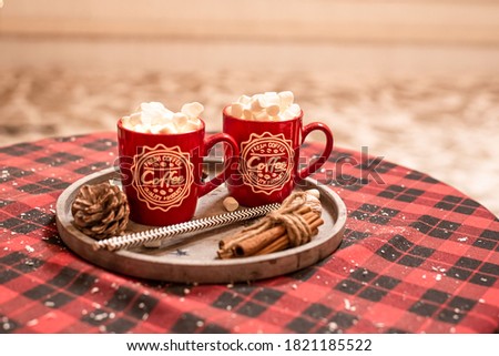 Hot cocoa with marshmallows in a Christmas red cup on a red and black checkered tablecloth. Hot chocolate with white marshmalows in a New Year's red cup. Happy New Year 2020.