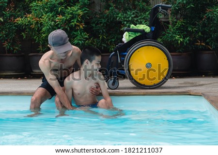 Strong arm muscles of Asian special child on wheelchair and father with swimming pool background, They are happiness in holidays with family time on the travel,Lifestyle of happy disabled kid concept.