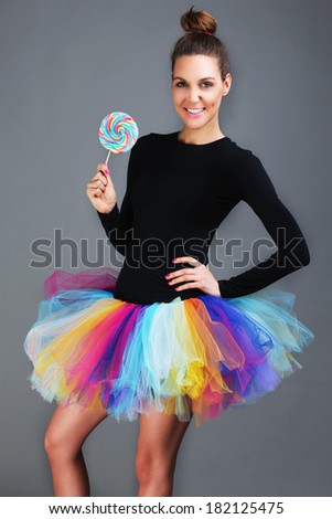 A picture of a happy fashionable woman posing with a lollipop over gray background